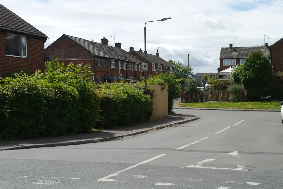 Quiet residential estate street with houses, hedges and a cloudy sky