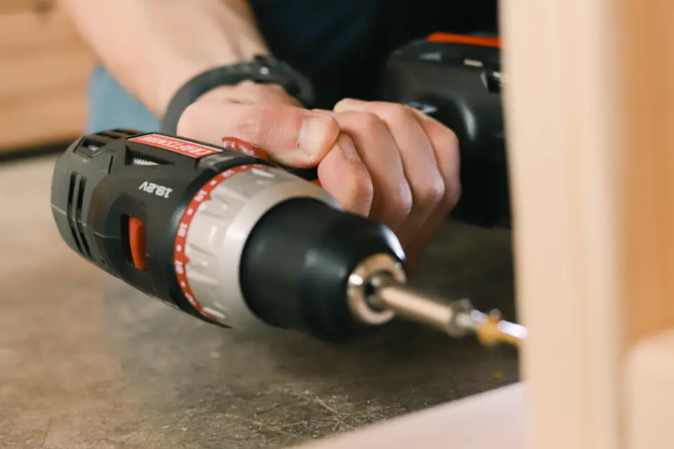 Cordless drill used for furniture assembly Close-up of a hand holding a cordless drill driving a screw into wood