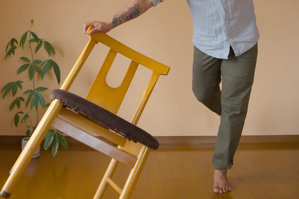 Man carrying a wooden chair through a room with a plant in the background