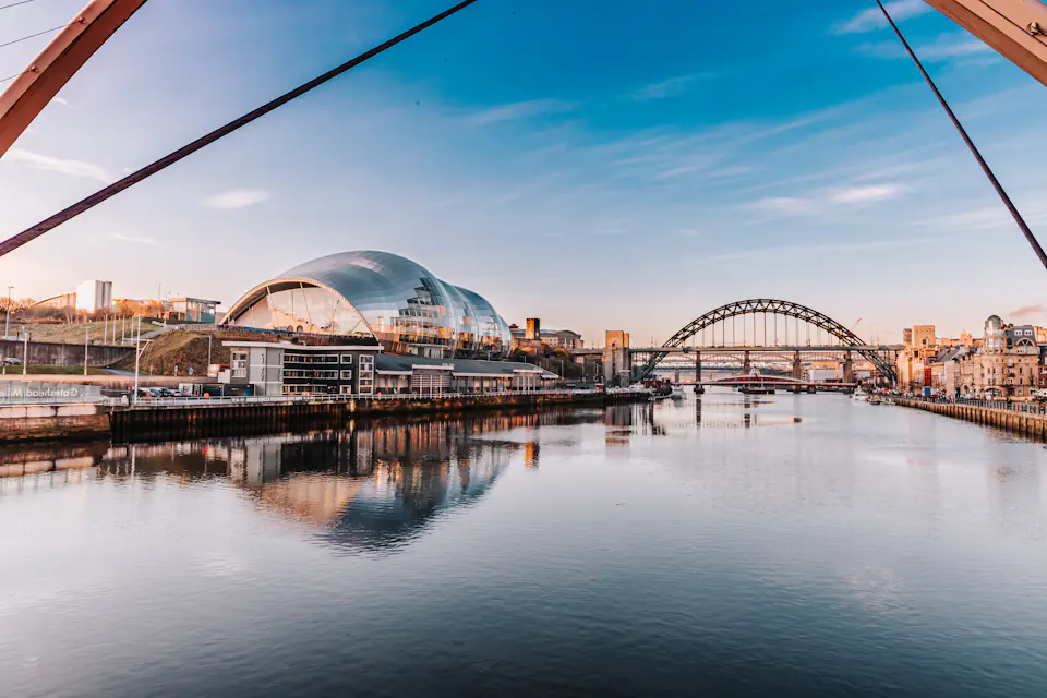 Gateshead Quays with the curved roof of The Glasshouse (formerly Sage Gateshead) and the Tyne Bridge reflected in the river