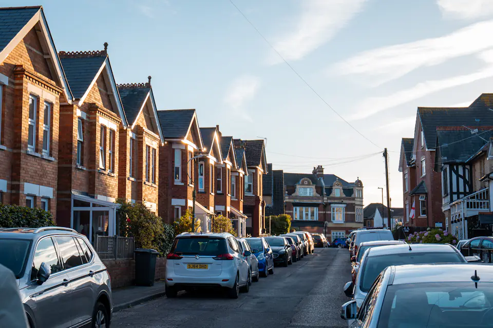 Red-brick terraced houses along a residential street lined with parked cars