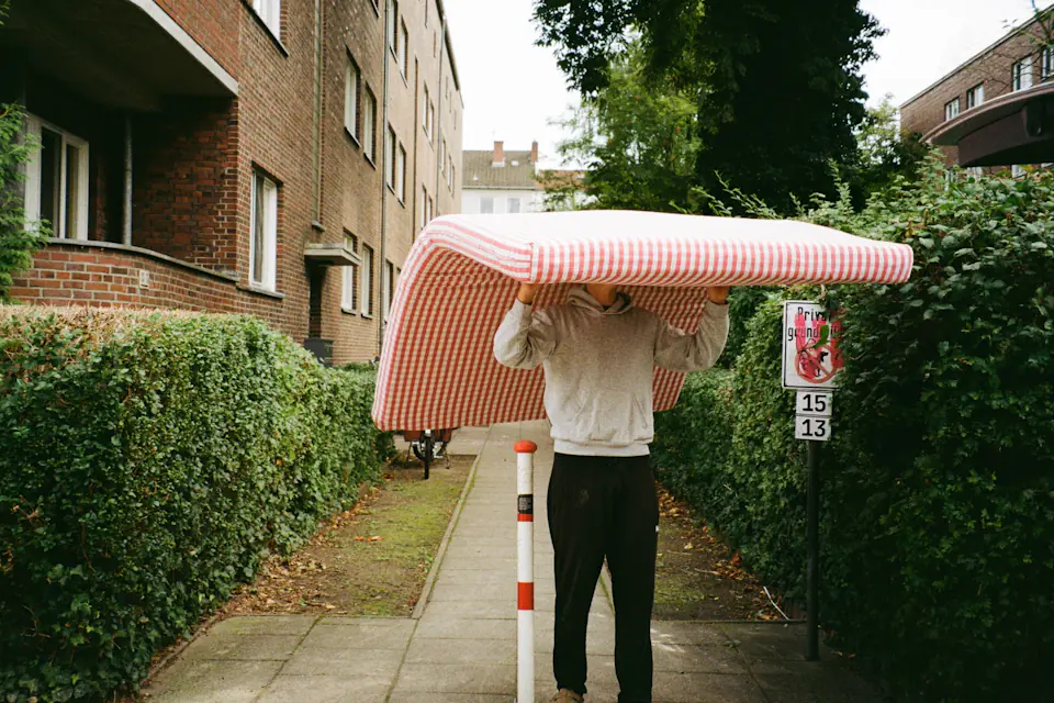 Person carrying a mattress over their head along a residential pavement