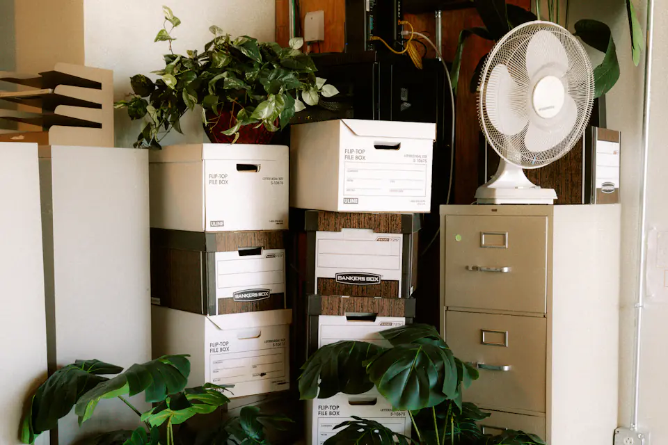 Office archive boxes packed for relocation Office corner with archive boxes stacked beside filing cabinets and plants