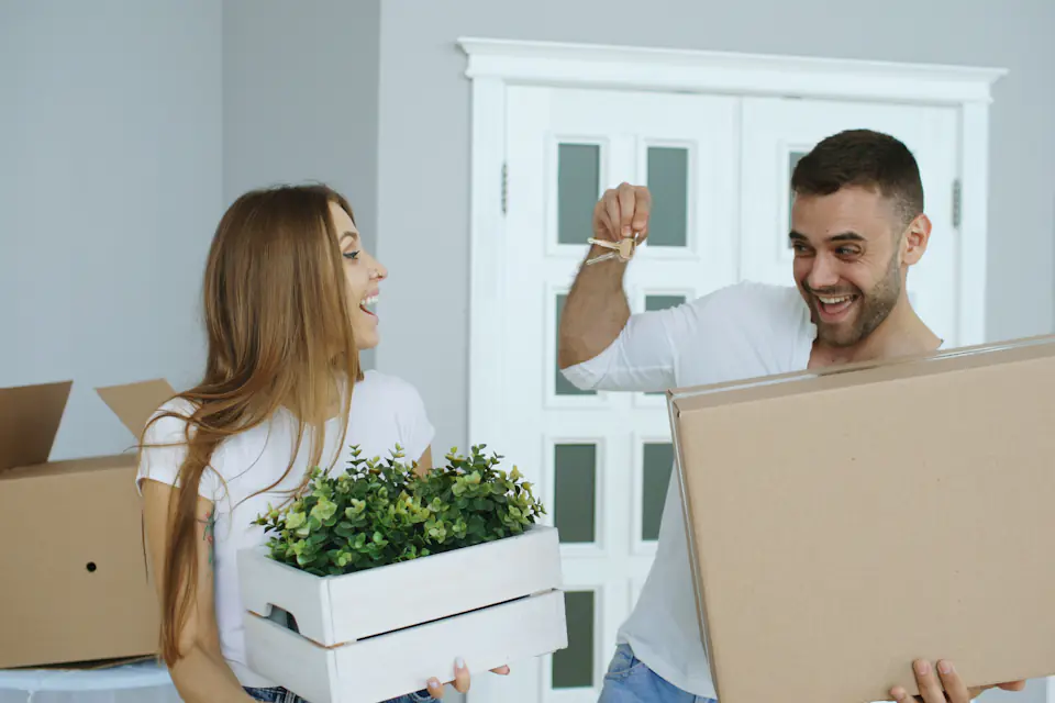 Happy couple arriving at their new home holding boxes and a planter